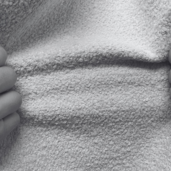 A close-up black and white image of two hands pulling at a textured upholstery fabric, testing its elasticity and durability.